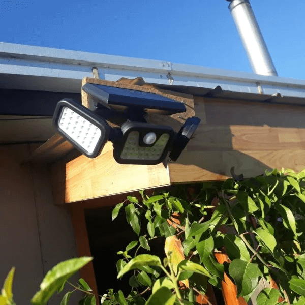 Three solar-powered LED light panels mounted on a wooden structure with green plants in the foreground.