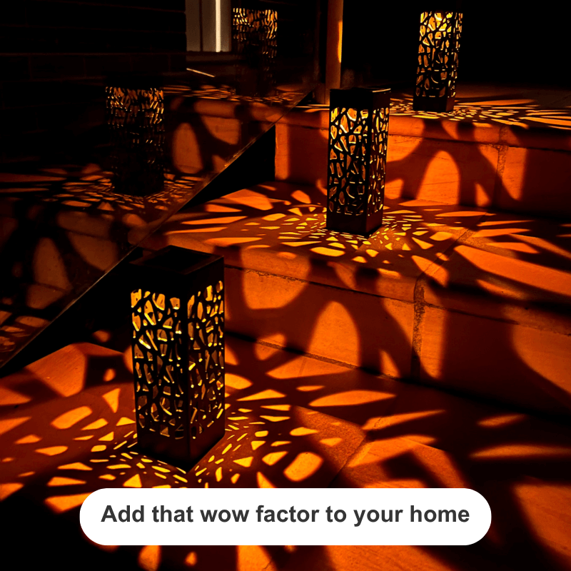Several tall black metal lanterns with intricate cutout patterns are placed on outdoor stone steps, casting dramatic orange and red shadow patterns across the surface. A white rounded text bubble at the bottom reads, 'Add that wow factor to your home'.