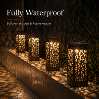 Four black metal outdoor lanterns with intricate cutout patterns, glowing with warm light on a wet stone ledge in the rain. White text at the top reads 'Fully Waterproof' and 'Built for rain, dew & Aussie weather'.