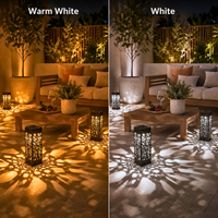 A side-by-side comparison showing outdoor patio lighting in two color modes: 'Warm White' on the left, casting a golden glow, and 'White' on the right, casting a bright white light. Both scenes feature a patio sofa, potted plants, a wooden coffee table, and decorative lanterns casting intricate leaf-shaped shadows on the tiled floor.
